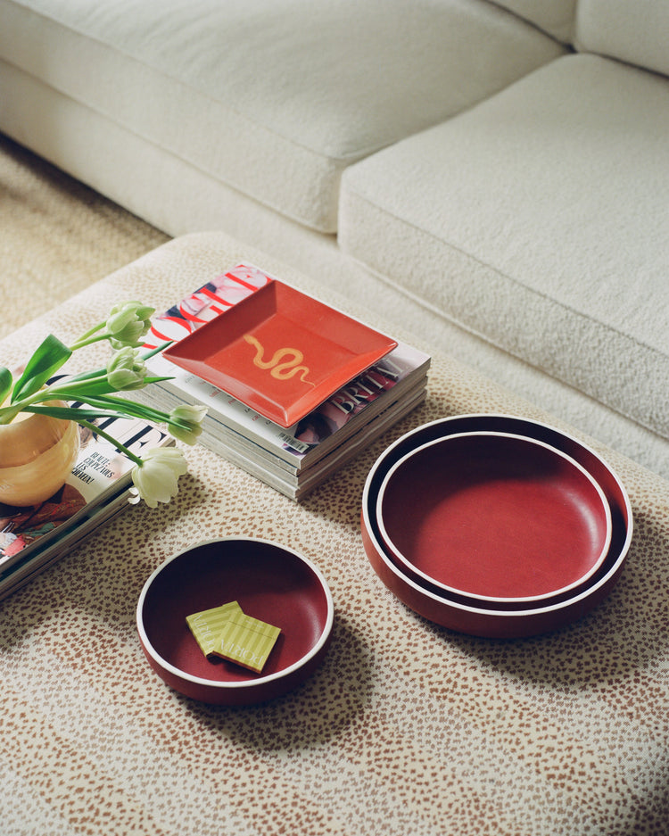 Two red ceramic bowls on a patterned table with a book stack and flowers nearby.