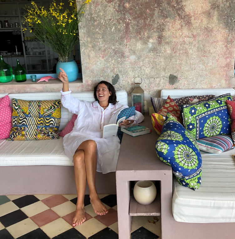 Woman sitting on a cushioned bench with colorful pillows, smiling and holding a book.