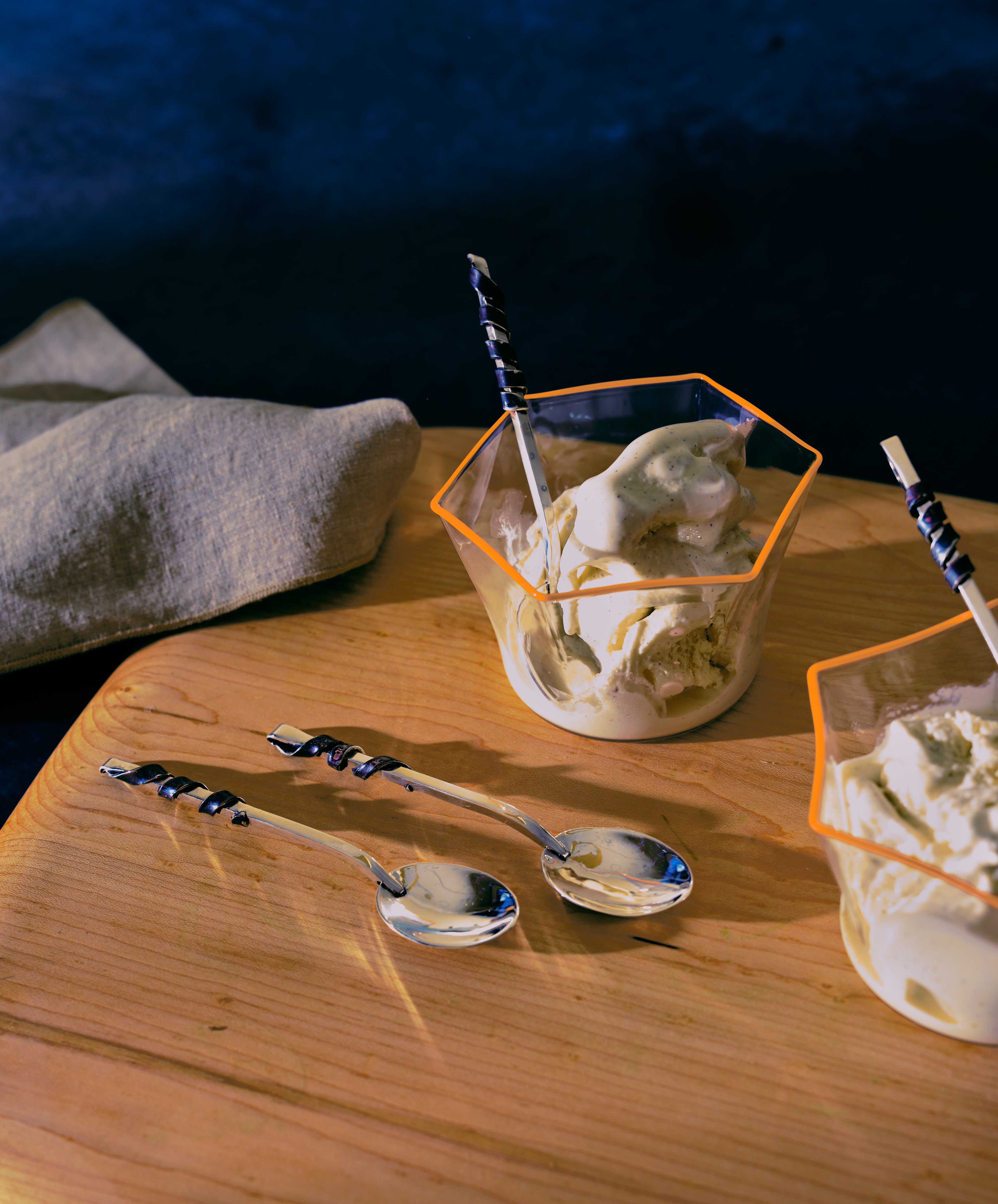 Set of silver ice cream spoons in situ on wood board and with ice cream from glass bowls.