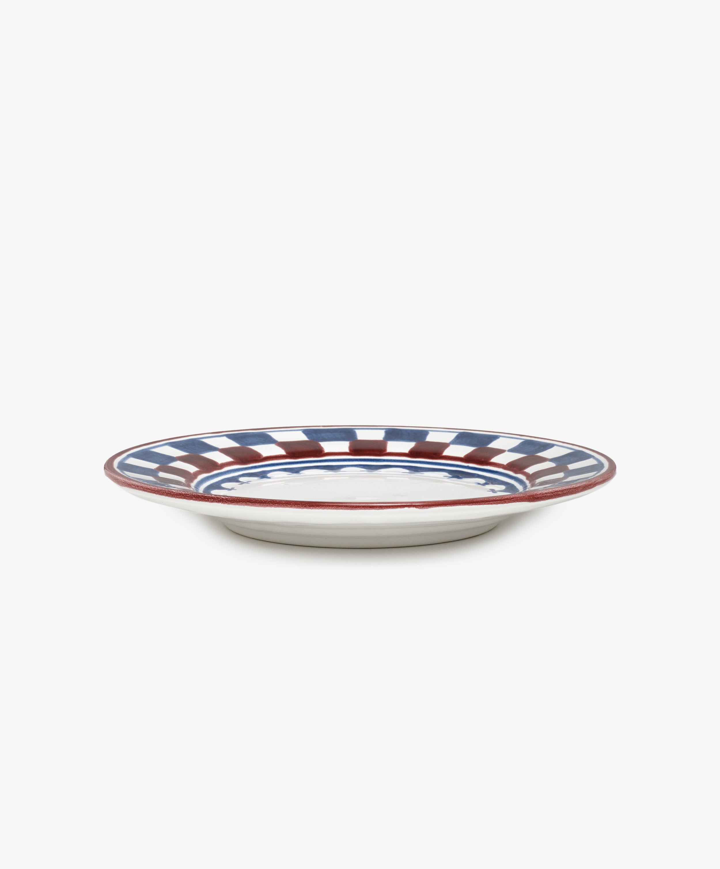 The Luca Small Plate, Set of 4, features a white ceramic base with hand-painted blue and red checkered and striped patterns around the rim, shown from a side view against a plain background.