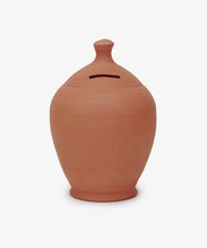 The Hugo Money Pot is a sculptural terracotta clay coin bank with a rounded body, small knob lid, and a horizontal slot for inserting coins.