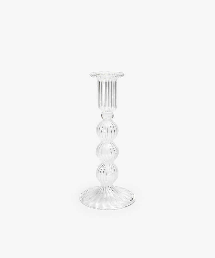 The Elsa Candleholder is a clear, hand-blown glass piece with a ribbed surface and round, tiered stem, expertly crafted by artisans and displayed against a plain white background.