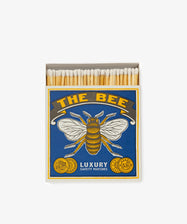 An open box of Luxury Matches featuring charming bee-themed matchbox art on a blue background with gold accents.