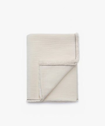 A neatly folded Filial Tablecloth in light beige with visible stitching and a hint of green branch stitch along the edge, displayed against a plain white background.