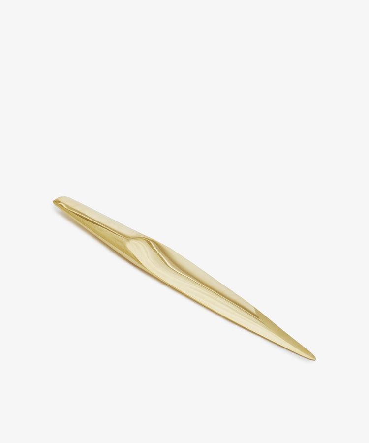 A gold-colored, elongated, and sleek metal Letter Opener—possibly solid brass or a sculptural desk accessory—photographed on a white background.
