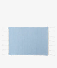 A set of six Gaia Placemats, rectangular and light blue with white fringe on the short sides, made from recycled fabric by Portuguese artisans, displayed on a white background.