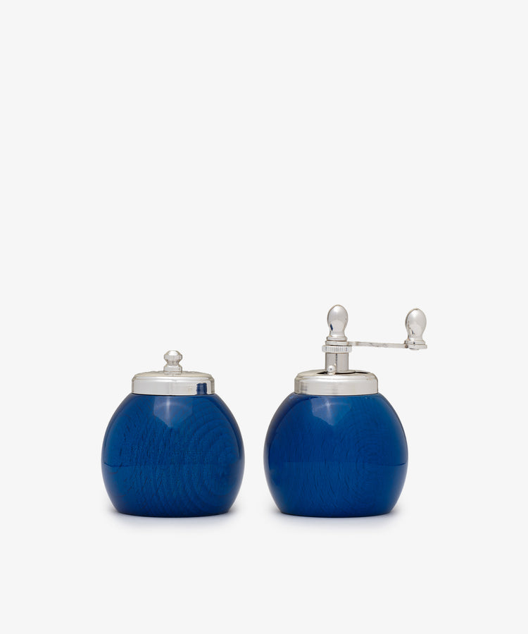 The Theo Pepper Mill and Salt Shaker set features two round, blue containers with silver lids; the right one has a grinder, while the left serves as a shaker—both exhibit classic Italian design.