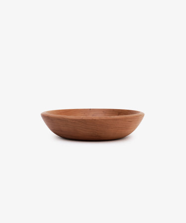 The August Wood Serving Bowl, a shallow, round piece hand-made from American dark cherry wood, sits on a plain white background.