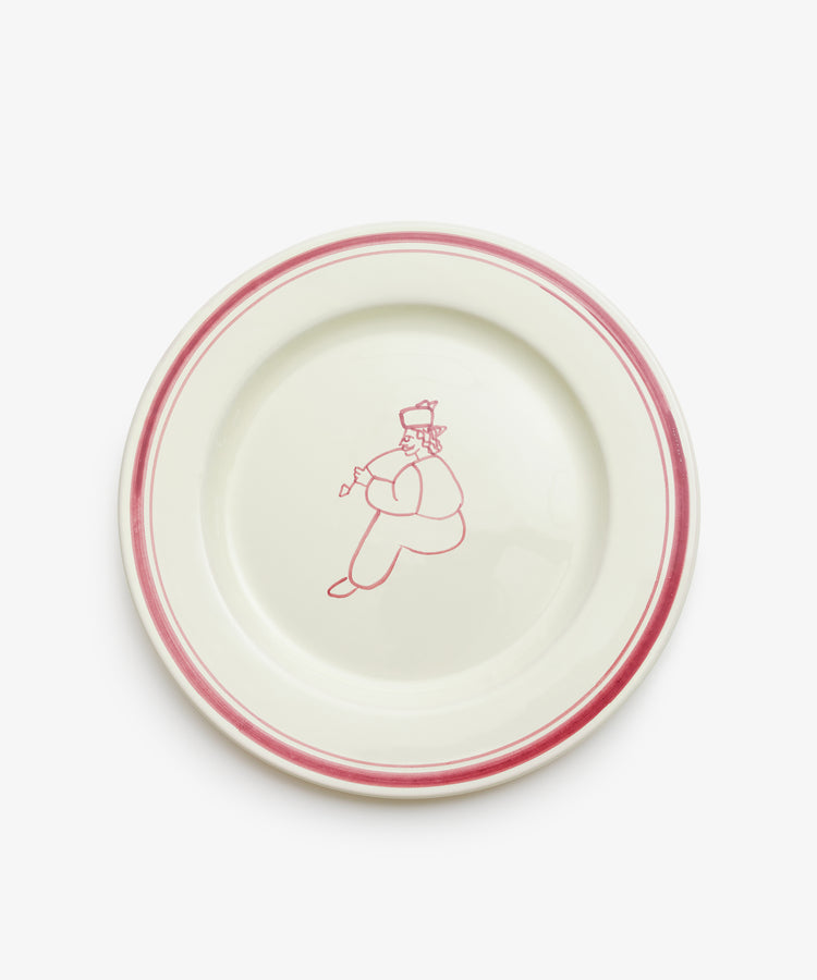The Folk Dinner Plate, Farmer is a white ceramic plate with a red rim and a minimalist red line drawing of a farmer holding an object in the center—an elegant hand-painted piece by an Italian ceramist.