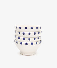 The Nina Bowl, Set of 4, features white ceramic bowls with blue polka dot patterns and a detailed dotted rim, shown stacked on a plain white background.