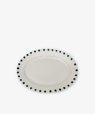 The Nina Oval Serving Platter is a hand-glazed ceramic plate with an oval shape and a border of evenly spaced black dots, perfect as an entertaining essential for stylish serving.