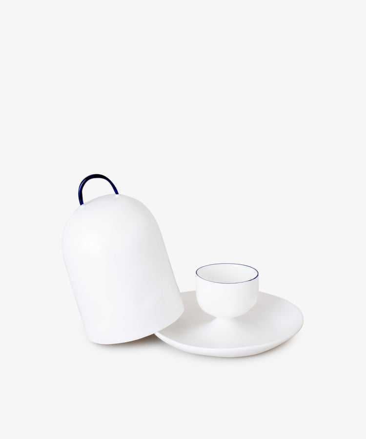 Egg Cup and Lid. White china domed lid with rounded black handle sits on angle against egg cup with thin black border.