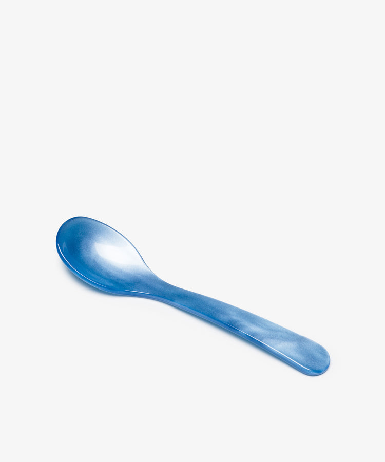 The Piccolo Spoon, made from blue acrylic with elegant craftsmanship, rests on a plain white background.