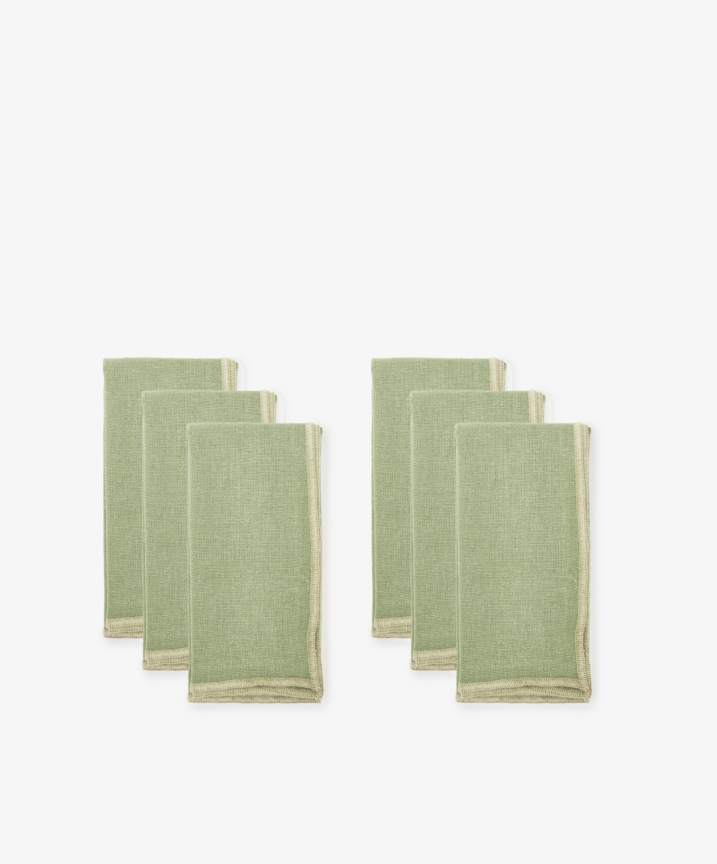 Set of six Corte Napkins in green linen with beige edging, eco-friendly, folded and arranged in two groups on a white background.