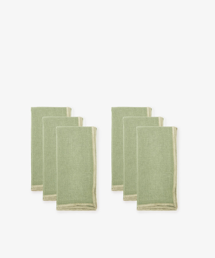 Set of six Corte Napkins in green linen with beige edging, eco-friendly, folded and arranged in two groups on a white background.