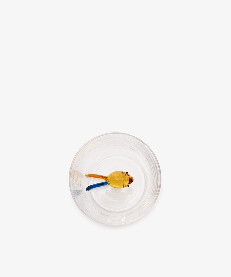 A yellow flower with a blue stem rests in an Ichendorf Milano Fish Tumbler (set of 2) made from borosilicate glass on a white background, viewed from above.