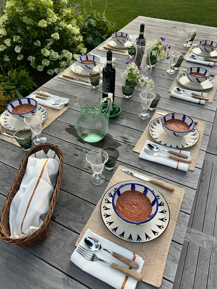 Elegant outdoor table setting with patterned plates, green glassware, and fresh flowers, bowls of soup