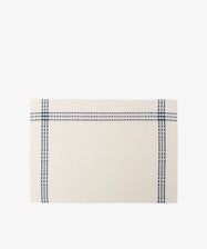 The Tilde Placemat, Set of 6, features a rectangular cream cotton-linen design with two intersecting blue stripes forming a cross near the edges, inspired by the classic Daldräll pattern and displayed on a white background.
