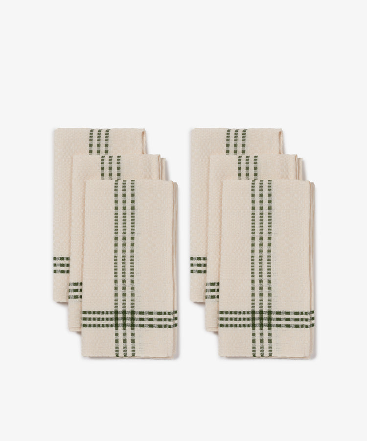 Six cream-colored Tilde napkins with green Daldräll stripes, made from a cotton and linen blend, are arranged in two neat stacks against a white background.