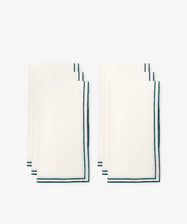 The Flavia Napkin Set of 6 features neatly folded linen napkins with dark green trim and a subtle double-line stitch, arranged in two groups of three on a plain white background.