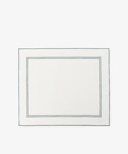 The Flavia Placemat, Set of 6, features rectangular white linen with two thin dark-bordered outlines near the edges—a refined and durable choice for elegant table settings.