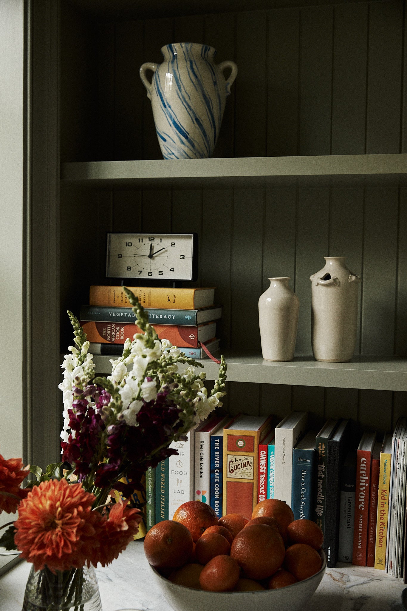 Bookshelf with decorative items including vases, a clock, and a bowl of fruit.