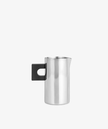 The S.R. Metal Pitcher features an elegant, sculptural stainless steel body with a flat black handle and spout, showcased against a simple light background.