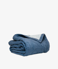 The Dawn Twin Bedspread, a folded blue quilt with subtle embroidered patterns that highlight Swedish craftsmanship, is displayed on a plain white background.