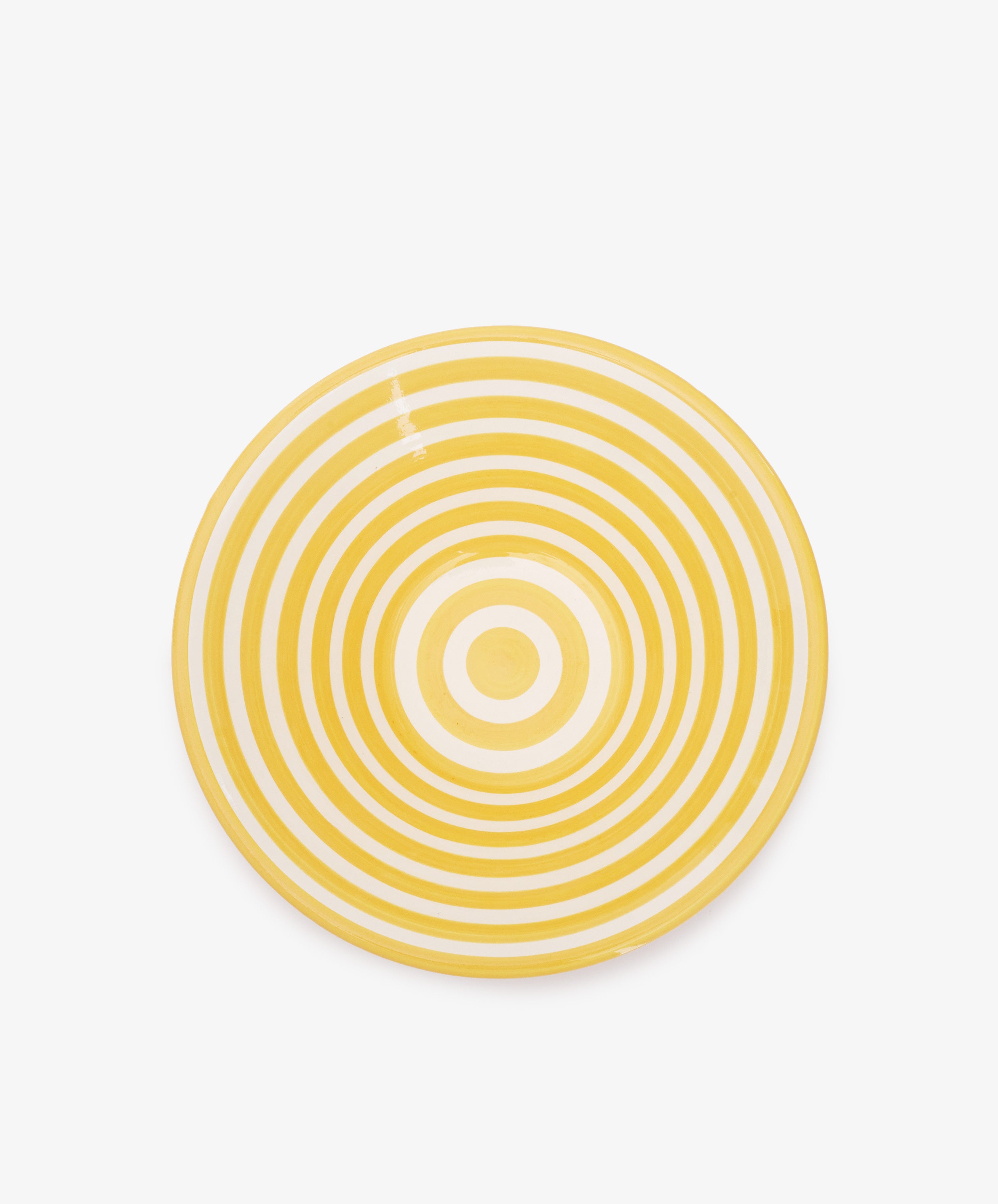 The Natalia Serving Bowl is a round, handmade piece with yellow and white concentric circles that stand out beautifully against a white background.