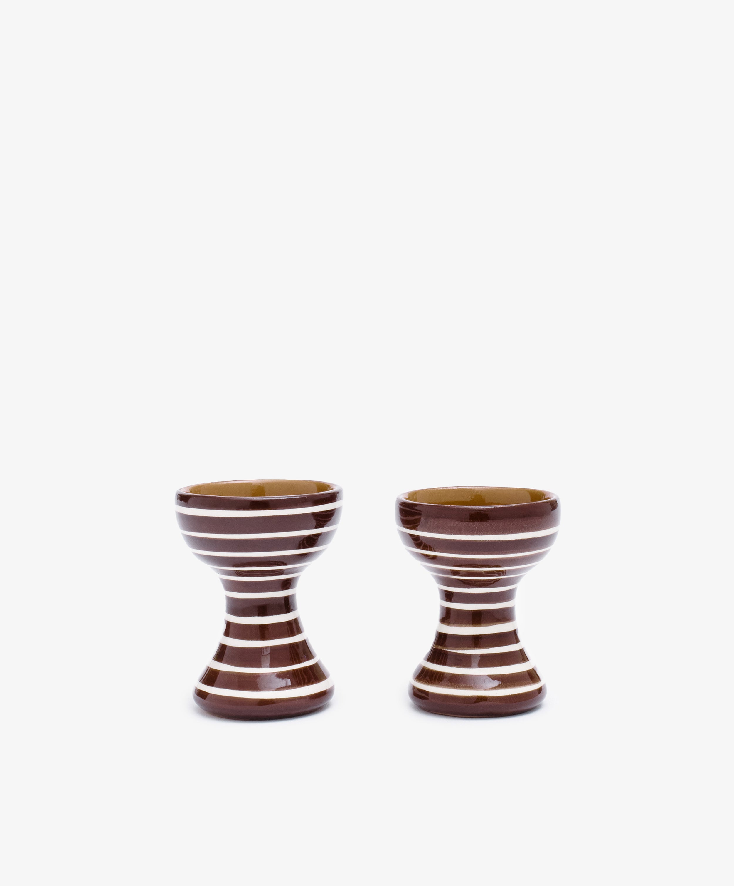 The Natalia Egg Cup, Set of 2, features handmade brown ceramic cups with white horizontal stripes, shown side by side on a white background—ideal for serving eggs and soldiers.