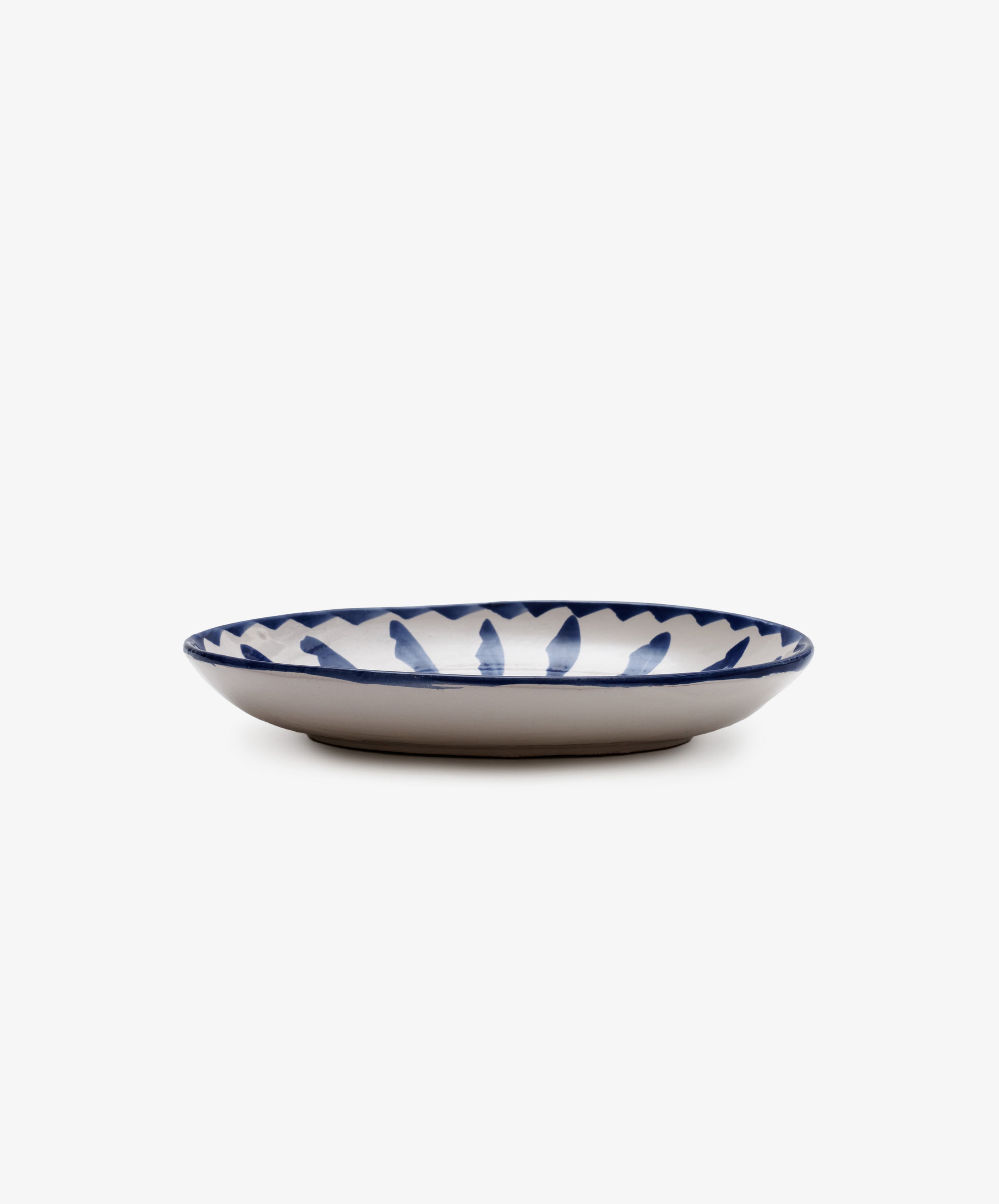 The Rayas Oval Serving Platter is a shallow handmade ceramic plate with a white base and a vibrant blue leaf-like rim pattern, shown against a plain white background.