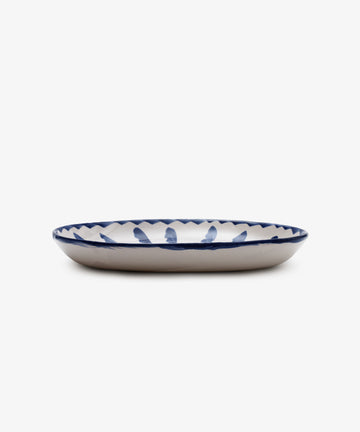 The Rayas Oval Serving Platter is a unique handmade ceramic plate featuring a white base and a vibrant blue hand-painted pattern around the rim, displayed against a white background.