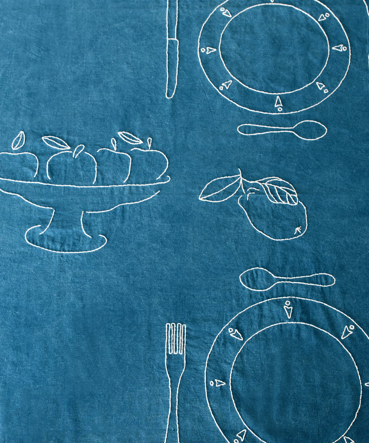 Close-up of white thread-embroidered fruit and table settings on Dîner d'Eté tablecloth in indigo linen.