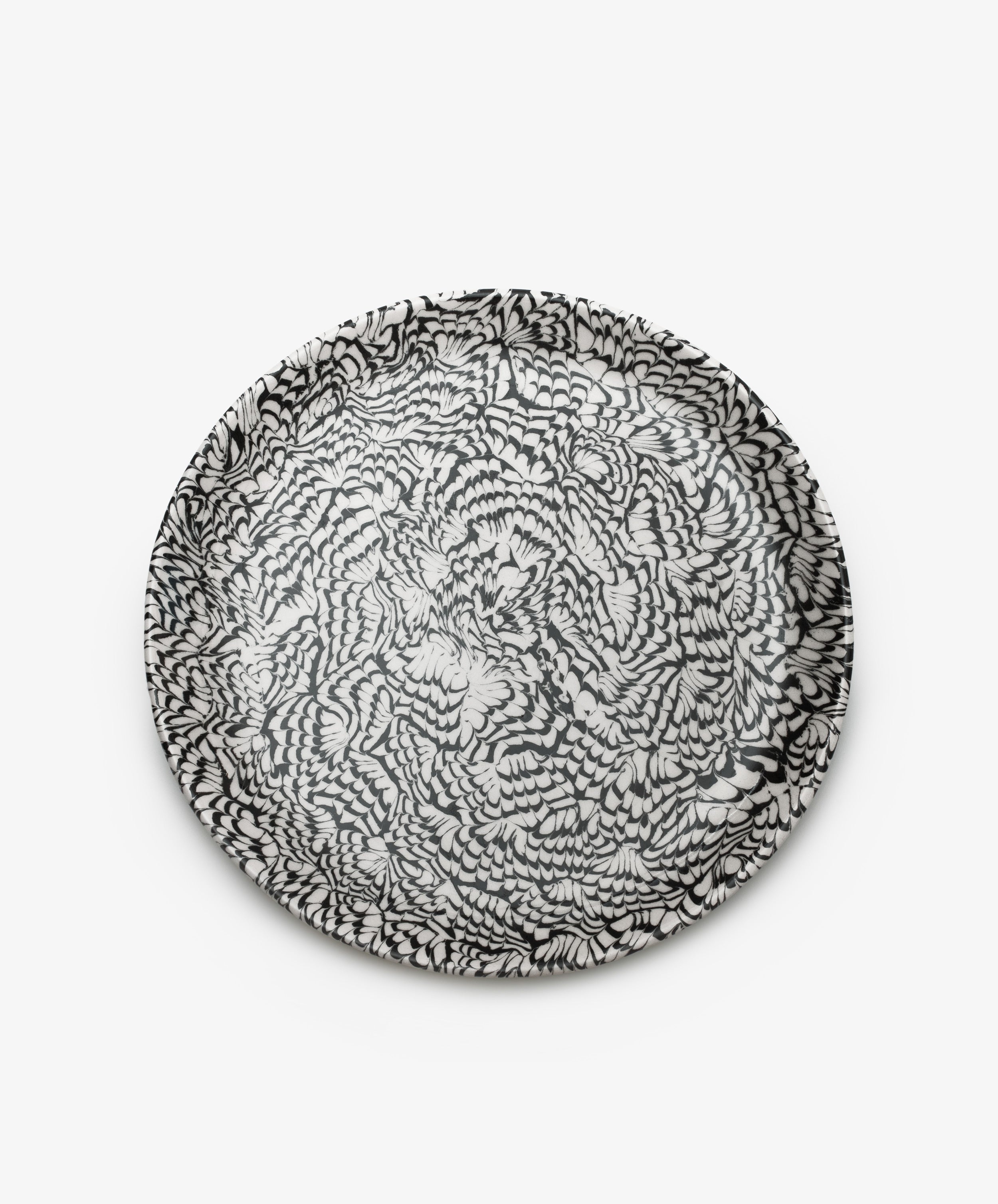 The Celine Serving Platter is a handcrafted round ceramic plate featuring an intricate black and white feather-like pattern on a plain white background.