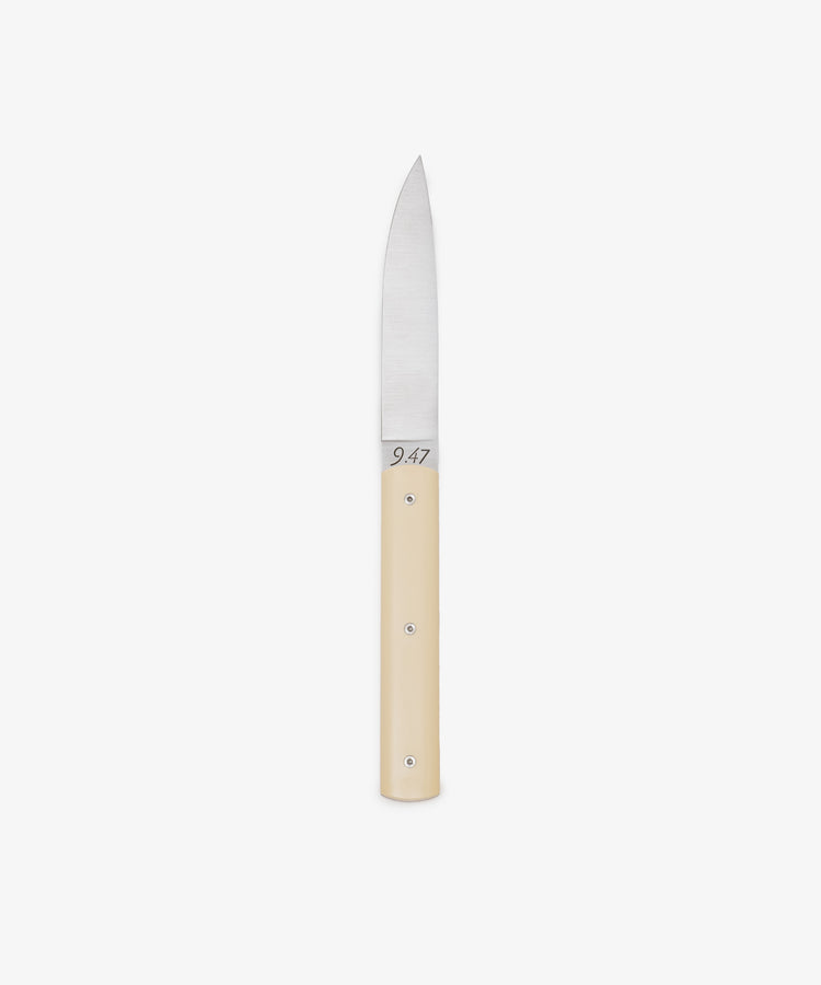 The 9.47 Table Knife features a straight, pointed steel blade and a smooth, light-colored handle, displayed against a white background to highlight its French craftsmanship inspired by the iconic Perceval 9.47.