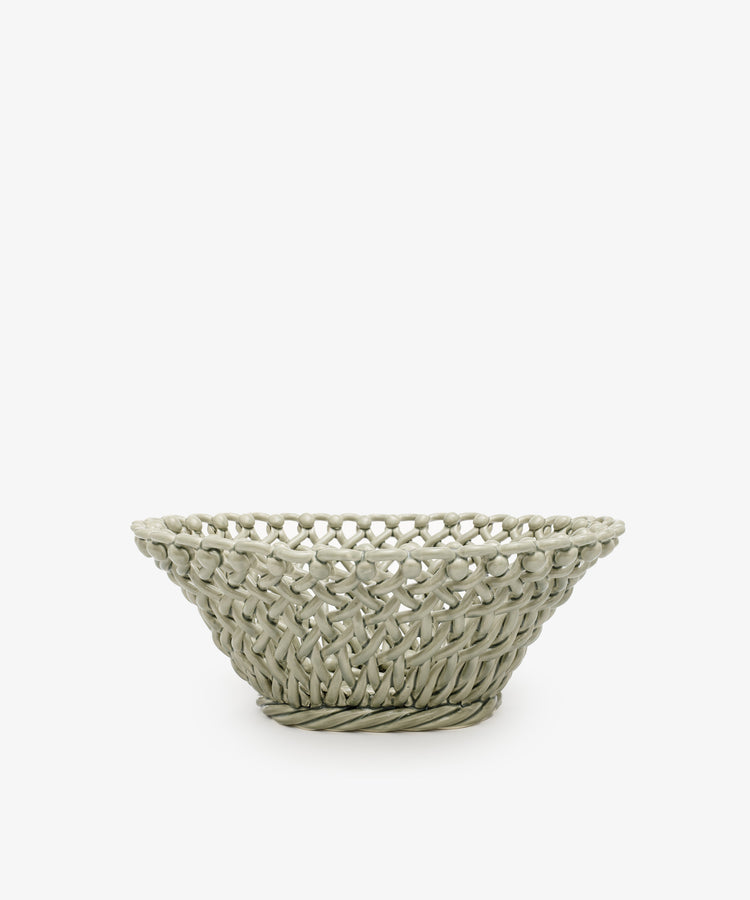 The Remi Decorative Fruit Bowl is a shallow, round, light gray ceramic basket with an open lattice design that makes a striking sculptural statement, shown here as a decorative accent against a plain white background.