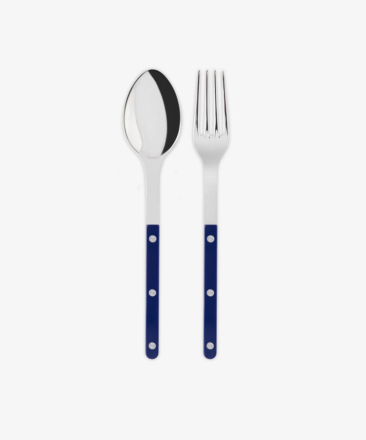 The Bistrot Serving Set features a metal spoon and fork with blue handles and three silver rivets, placed side by side on a white background, evoking Parisian bistro style.