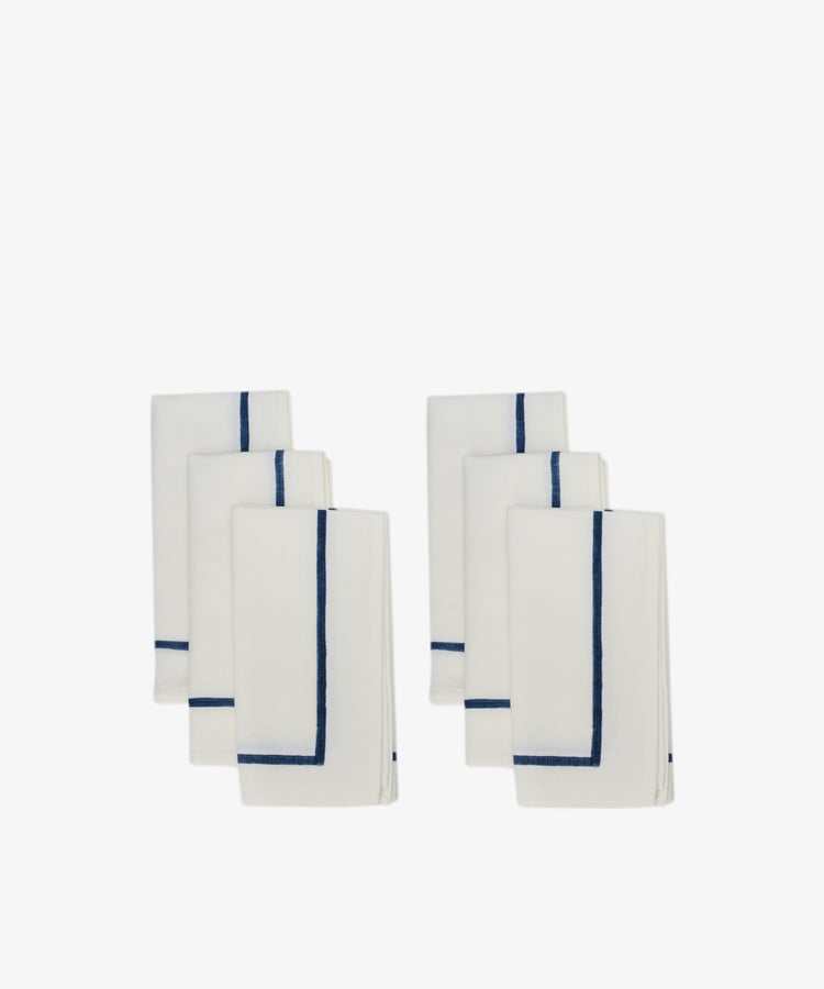 Six neatly folded Riga Napkins, Set of 6, in white with a simple dark blue border, arranged in two groups on a plain white background.