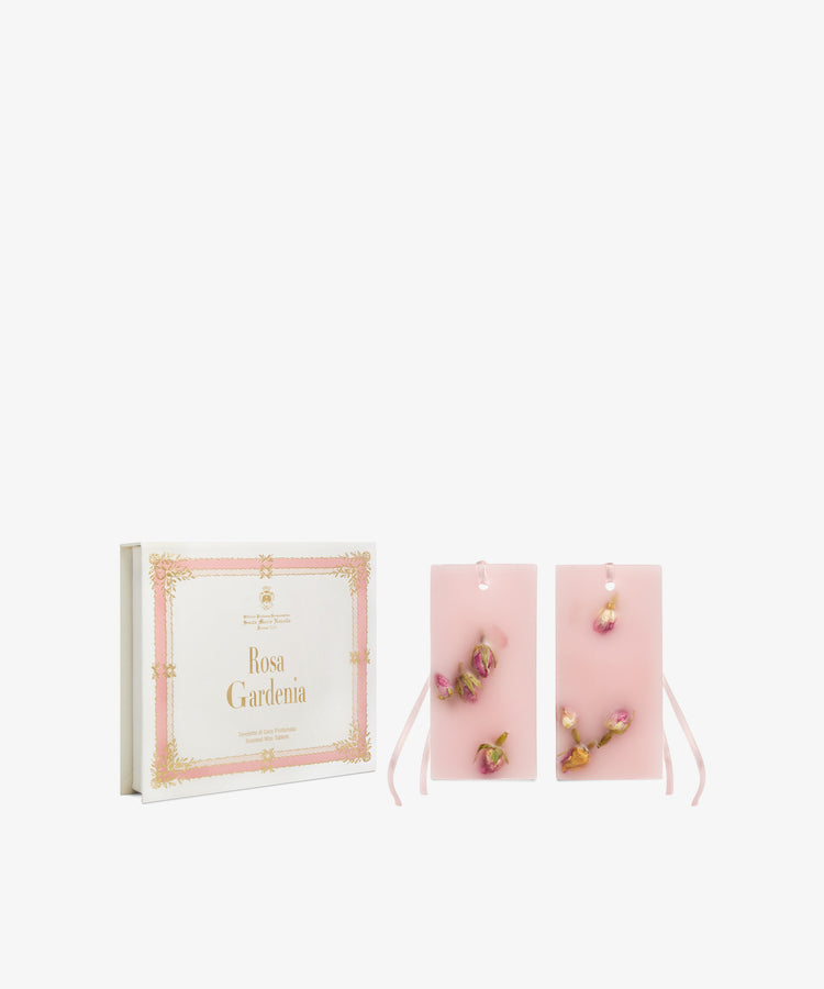A decorative box labeled Rosa Gardenia Scented Wax Tablets, Set of 2, sits next to two pink scented wax tablets with dried rosebuds and ribbons on a white background.