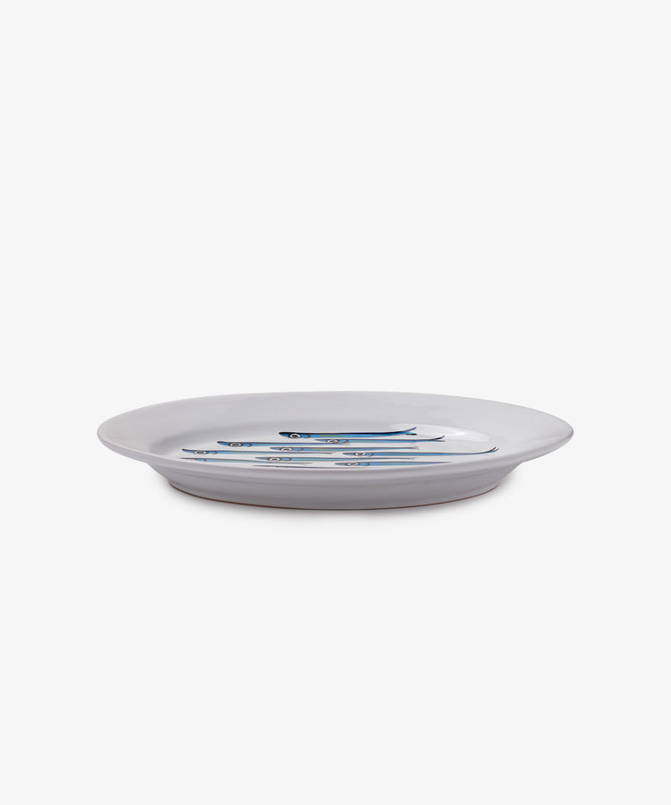 The Tommaso Oval Platter is a white ceramic plate featuring three blue and silver sardines at the center, inspired by the Amalfi Coast, set against a plain white background.