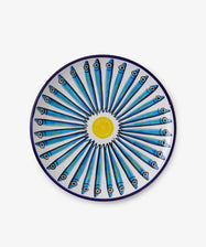 The Tommaso Platter is a round ceramic plate featuring a blue border and a radial pattern of blue sardines facing outward from a yellow center, capturing the vibrant charm of the Amalfi Coast.