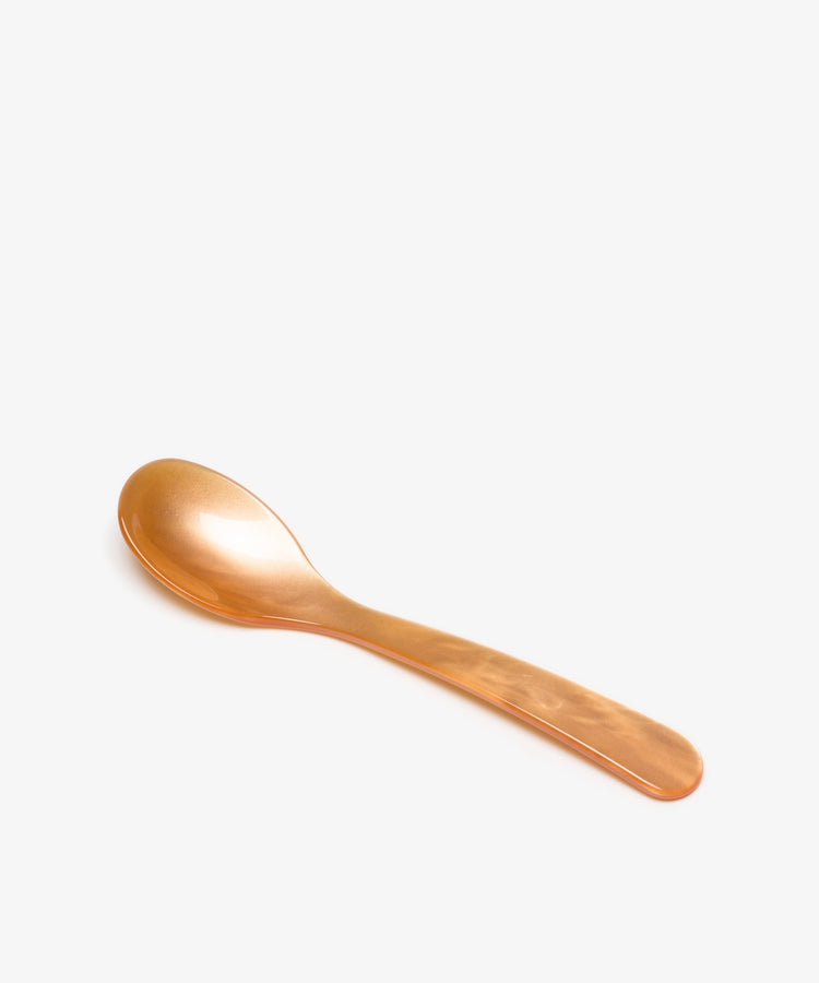 A Piccolo Spoon in orange acrylic is displayed on a plain white background, highlighting its simple design.