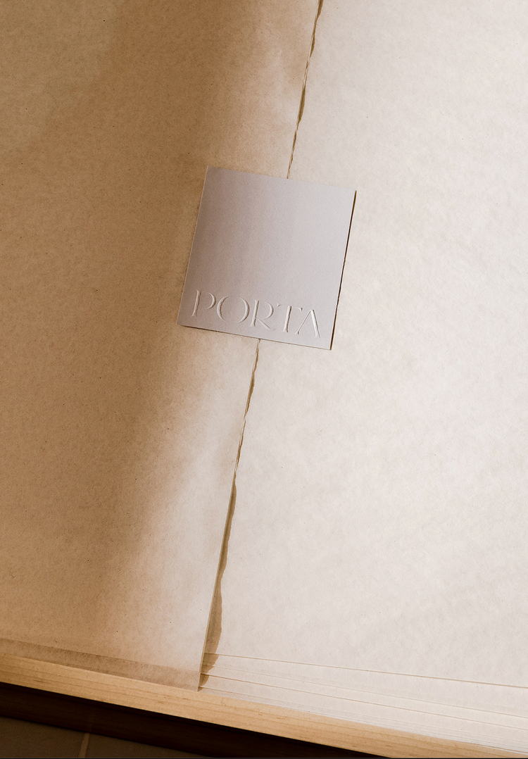 A beige card embossed with PORTA rests on the center of an open book with textured, cream-colored pages.