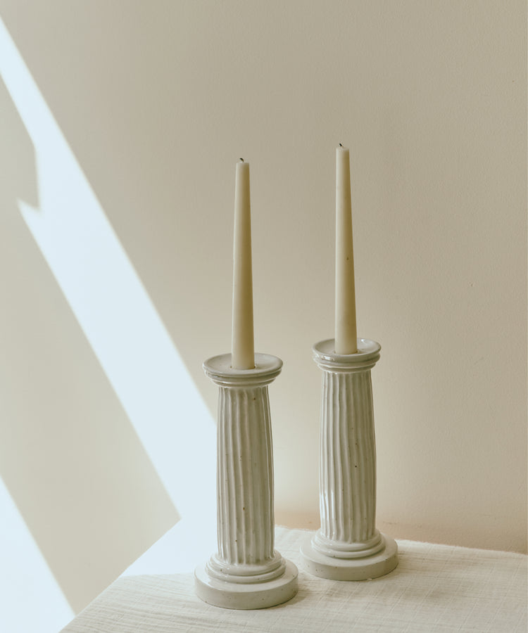 A Gift Card lets you shop beautiful items like two tall, unlit white taper candles in fluted ceramic holders—perfect for gifting or redeeming at checkout.