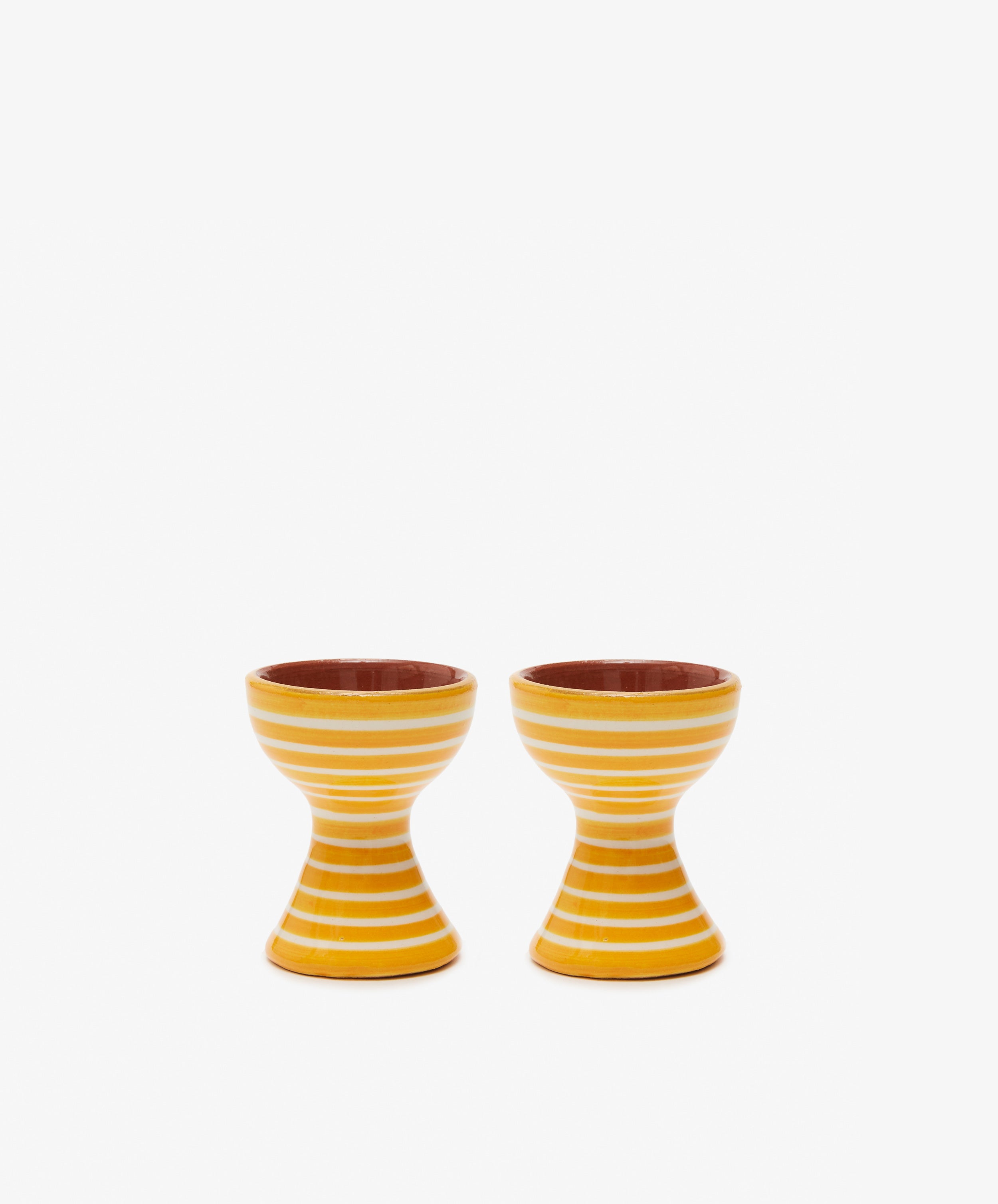 The Natalia Egg Cup, Set of 2, features yellow and white stripes and an hourglass shape—perfect for serving eggs and soldiers—bringing handmade charm to your breakfast table.