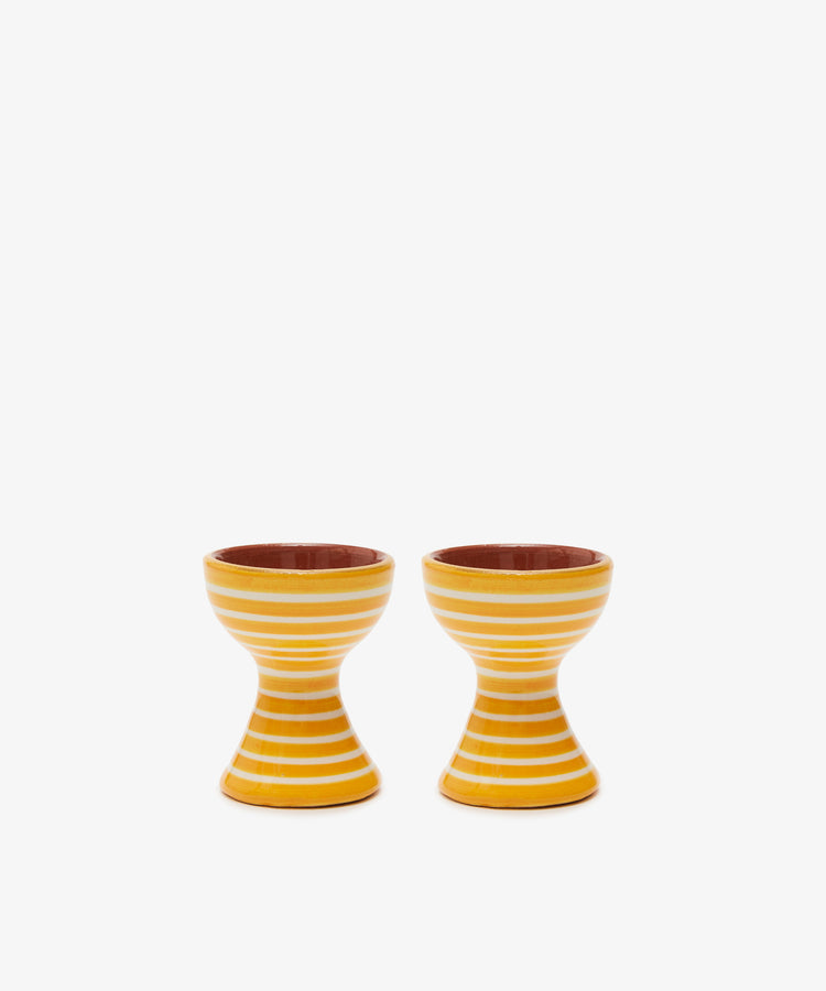 The Natalia Egg Cup, Set of 2, features yellow and white stripes and an hourglass shape—perfect for serving eggs and soldiers—bringing handmade charm to your breakfast table.