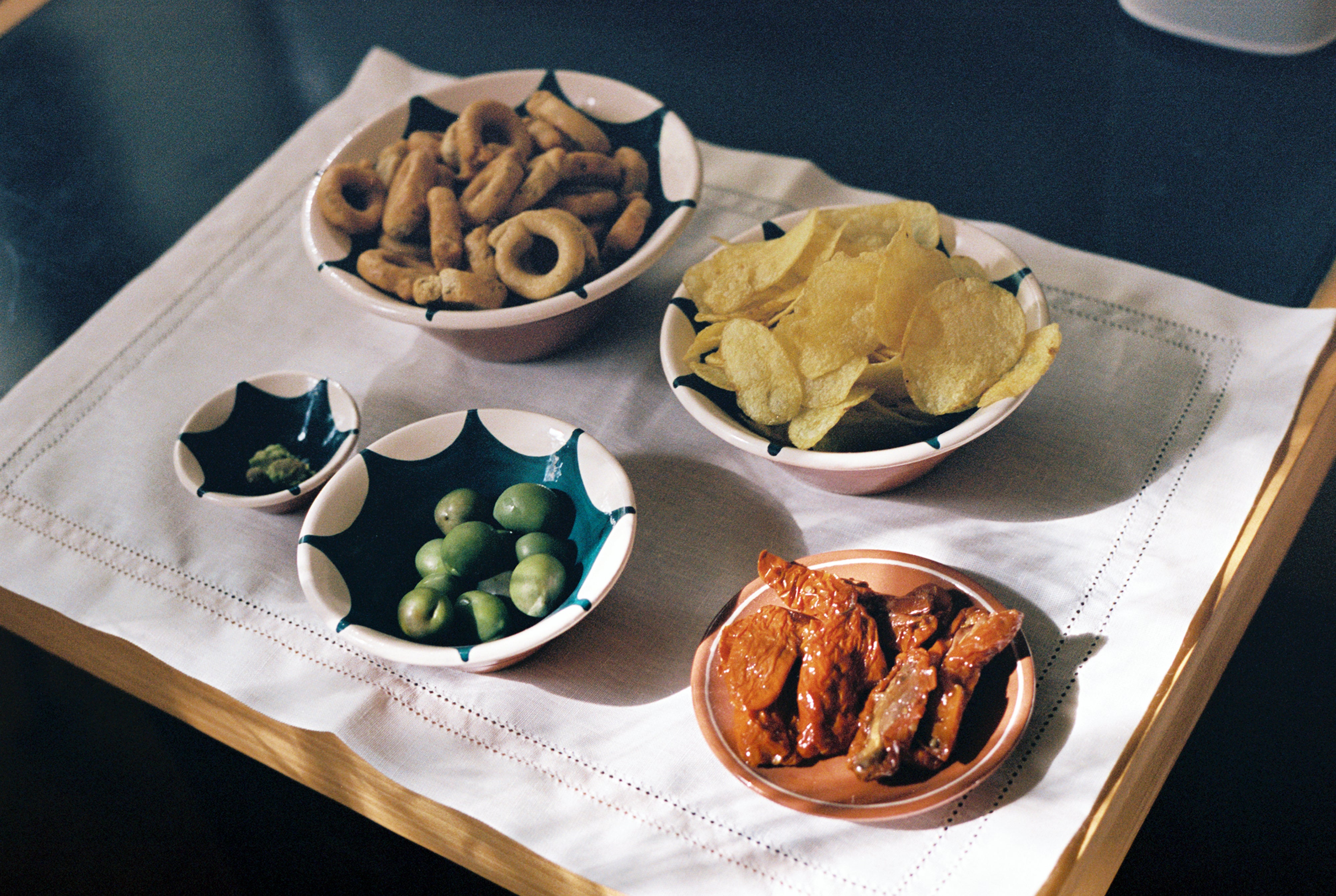 Lorna Hemstitch Placemat sits on table and holds various ceramic bowls of snacks.