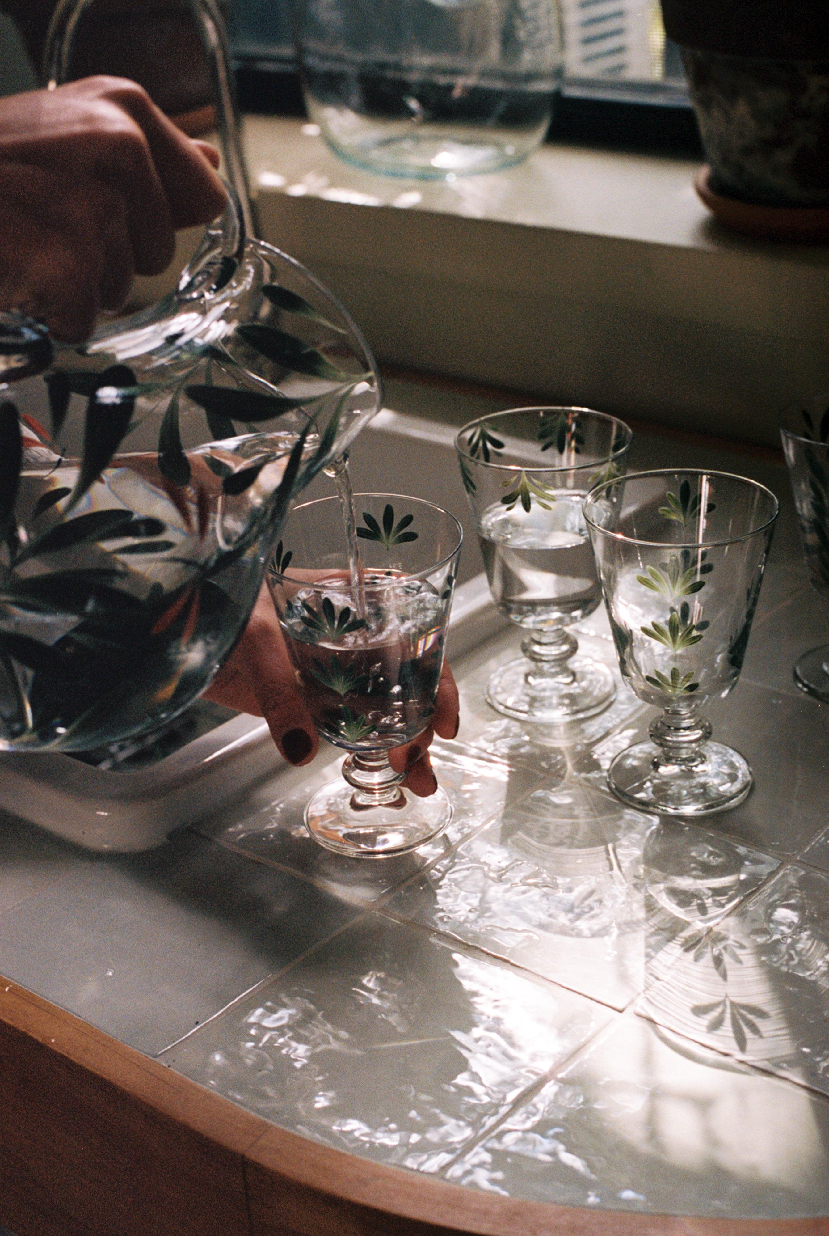 Dragonfly pitcher being used to pour water into painted glasses at sink.