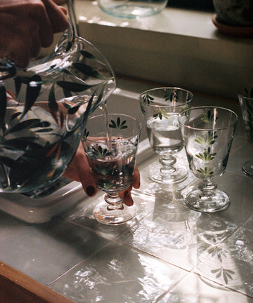 Dragonfly pitcher being used to pour water into painted glasses at sink.