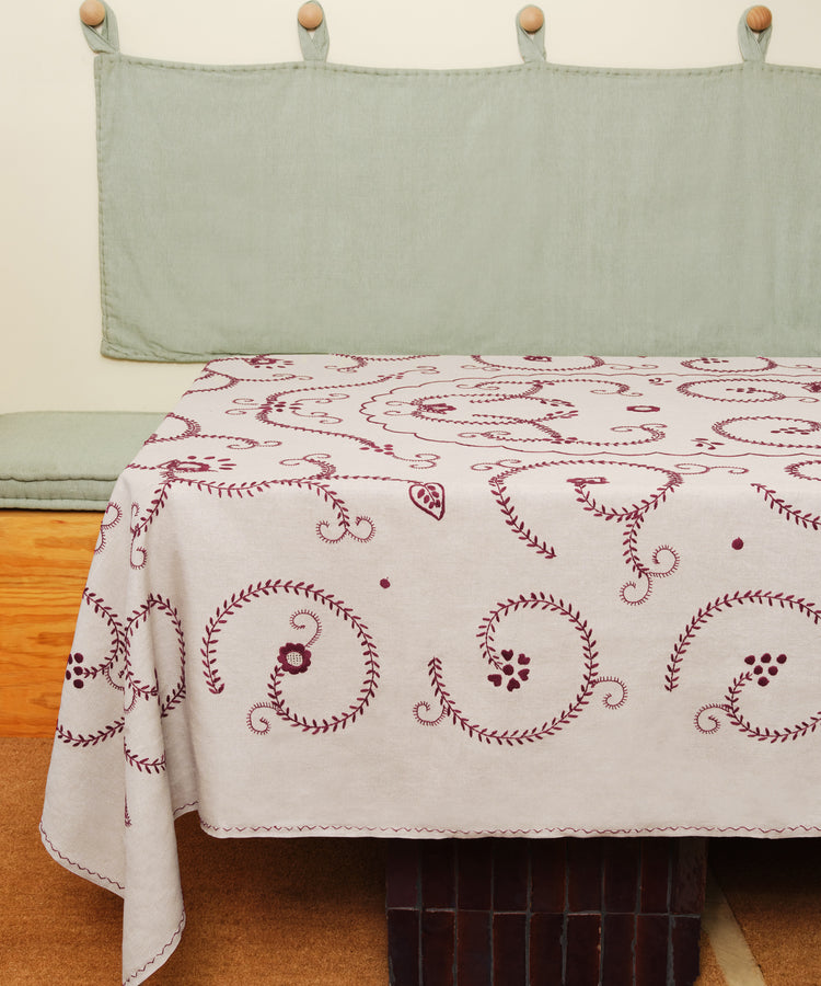 Tan and red Inez Tablecloth in situ, spread over table with green wall hanging and bench.